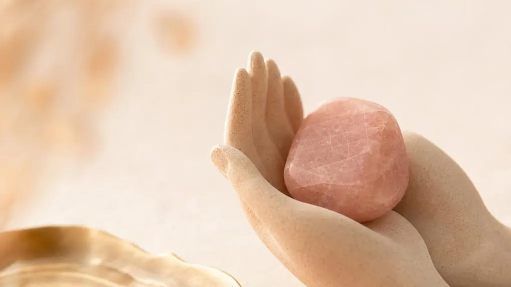 Zwei offene Hände halten locker einen glatten, roséfarbenen Stein mit natürlich unregelmäßiger Form.