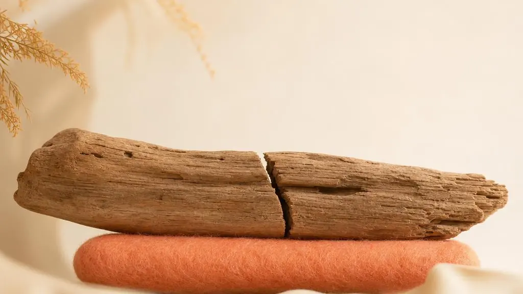 Ein gespaltenes Stück verwittertes Holz liegt sicher auf einem weichen Filzband, die Bruchstelle bleibt sichtbar.